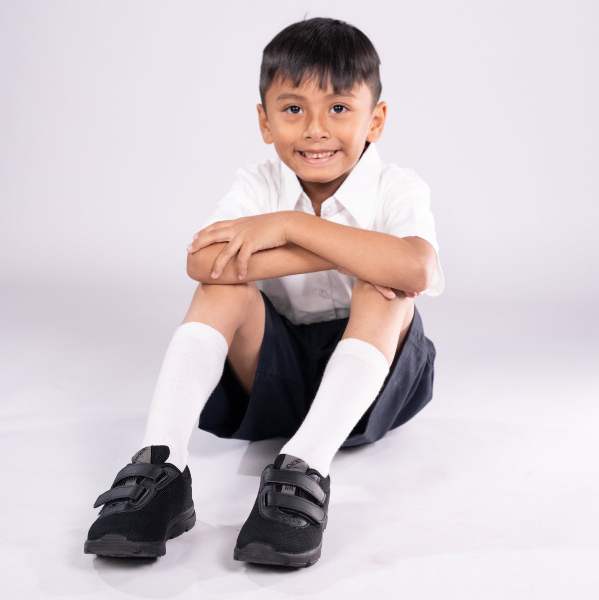 Child wearing a white shirt, dark shorts, and black shoes on a white background
