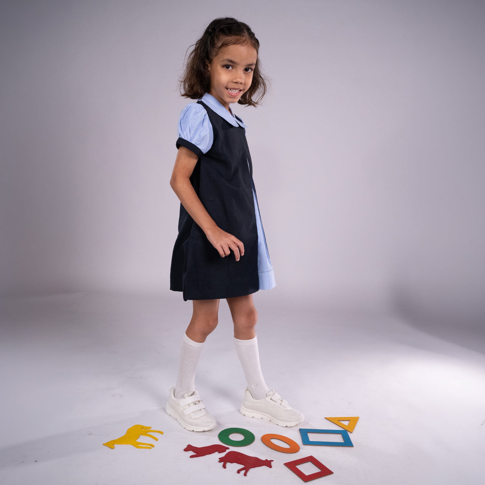 Young girl in a school uniform standing on a white background with educational shapes below her.