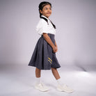 Young girl wearing a white shirt and gray skirt with a yellow detail on a plain background